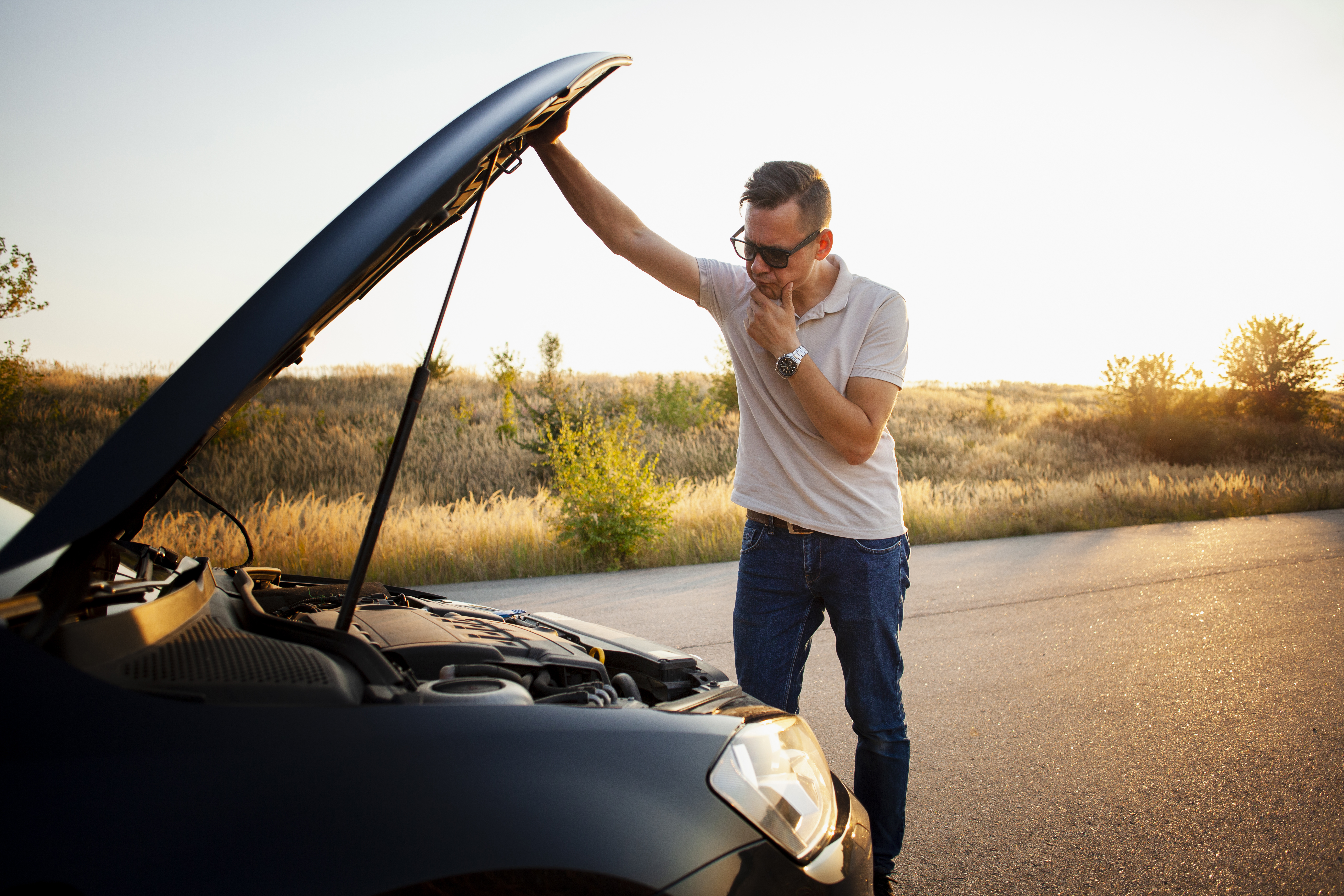 A imagem mostra um carro com capô aberto e um homem olhando para as peças